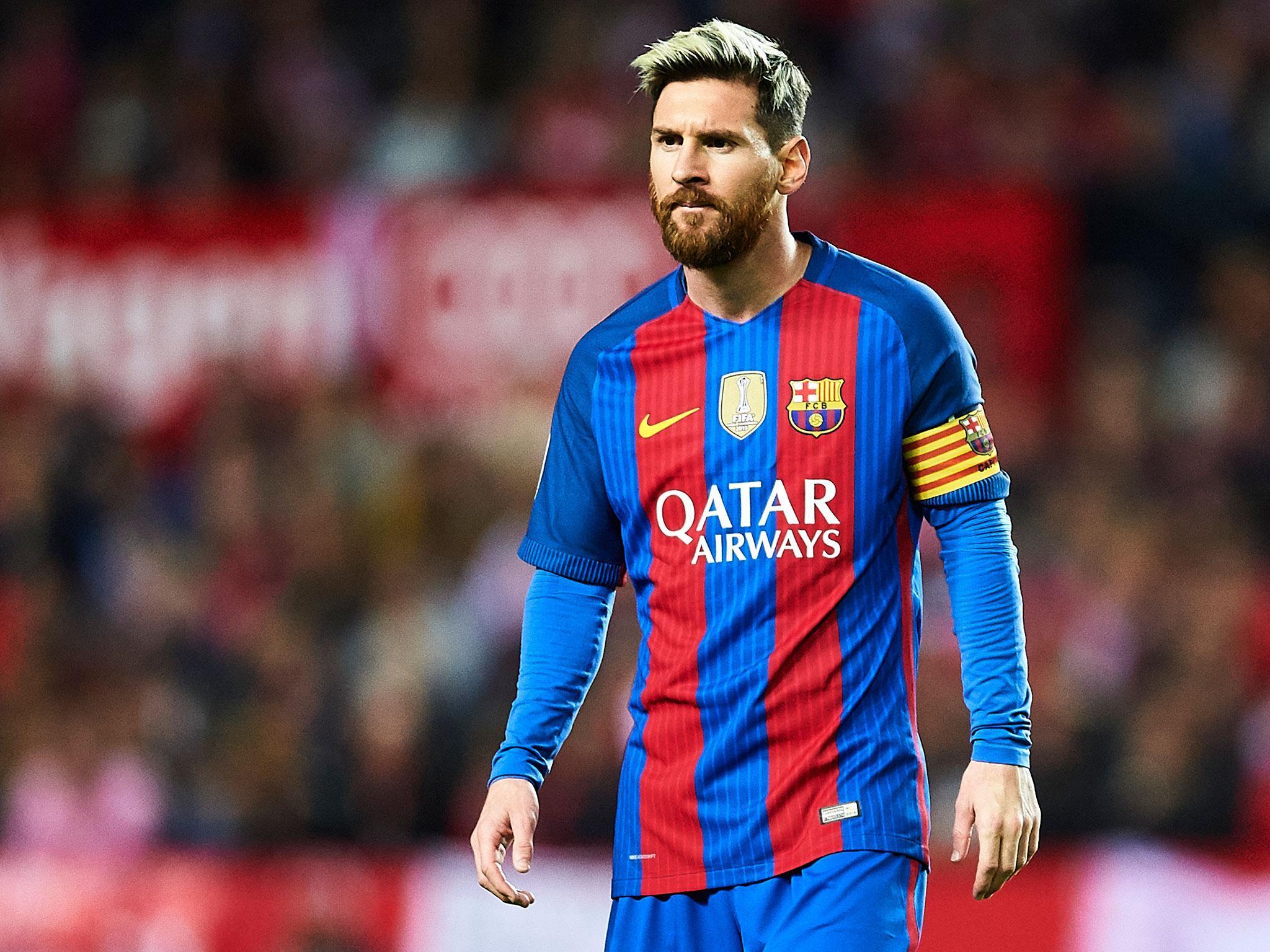 Seorang pesepak bola profesional mengenakan jersey Barcelona dengan ban kapten, menundukkan kepala sambil memegang bola Liga Champions di tengah stadion yang diterangi lampu malam.Lionel Messi